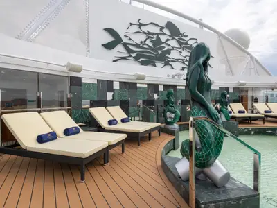 Ein luxuriöser Poolbereich an Bord der MSC Seaview, mit mehreren smaragdgrünen Meerjungfrauen-Skulpturen, Sonnenliegen und einem modernen Design.