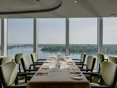 Elegantes Restaurant an Bord der MSC Seaview. Gedeckte Tische, hellgrüne Stühle, große Fensterfront. Weitblick auf eine Bucht mit Yachten und grüne Küstenlandschaft.