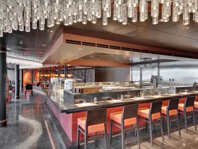 Innenansicht der Asian Market Kitchen Sushi Bar an Bord der MSC Seaview mit Thekenbestuhlung, offener Küche, modernen Möbeln und asiatischem Dekor.