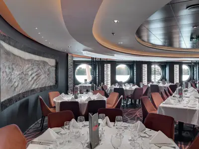 Das elegante Restaurant "Golden Sand" an Bord der MSC Seaview zeigt zahlreiche gedeckte Tische und weinrote Stühle. Große Portholes und eine reliefartige Wandkunst prägen die moderne Inneneinrichtung.