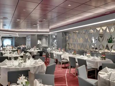 Das geräumige Hauptrestaurant Silver Dolphin an Bord der MSC Seaview zeigt gedeckte Tische, graue Stühle, roten Teppich und moderne Wandpaneele. Es ist hell und ohne Personen.