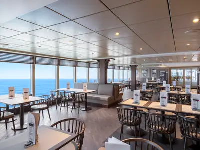 Ein heller Restaurantbereich an Bord der MSC Seaview, Ocean Point Restaurant & Buffet. Zahlreiche Tische, Stühle und Sitzbänke mit großen Panoramafenstern zum Meer.