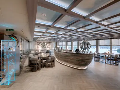Modernes Ocean Cay Restaurant an Bord der MSC Seaview. Elegante Tische, Bootsbar, Meerblick durch Panoramafenster. Maritime Kunst und ein Deckenraster mit Himmelmotiv.
