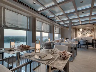 Ein elegantes Restaurant an Bord der MSC Seaview mit grossen Fenstern, die einen weiten Blick auf das Wasser bieten. Das moderne, maritime Design umfasst eine Fisch-Mosaikwand, stilvolle Deckenleuchten und schön gedeckte Tische.