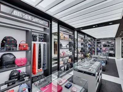 Blick in einen modernen Accessoires-Shop an Bord der MSC Seaview. Schwarze Regale präsentieren Designer-Handtaschen, Rucksäcke, Gürtel und Seidentücher unter heller Deckenbeleuchtung.