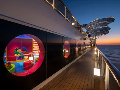 Die MSC Seaview bei Sonnenuntergang. Deck mit Bullaugen, eines zeigt einen Lego-Kinderbereich. Blaue Wasserrutschen ragen ueber das Meer.