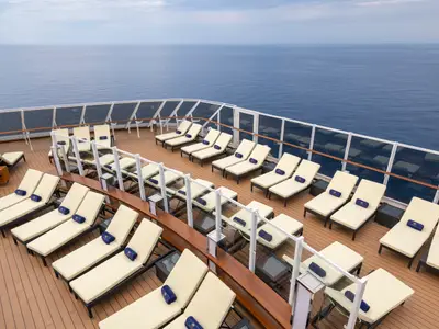 Ein weitläufiges Sonnendeck an Bord der MSC Seaview mit Reihen cremefarbener Liegestühle und blauen Handtüchern, die den Blick auf das offene Meer freigeben. Eine Glasbalustrade sichert den Bereich.