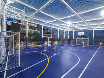 Blick in die helle, überdachte Multi-Sport-Arena an Bord der MSC Seaview. Der blaue Sportplatz ist mit weißen Linien für Basketball und gelben Linien für Fußball markiert. An den Enden stehen zwei Basketballkörbe und zwei Fußballtore. Die Arena ist von Netzen umschlossen, und darüber spannt sich ein weißes Netzdach. Im Hintergrund sind Außenbereiche des Schiffs erkennbar.