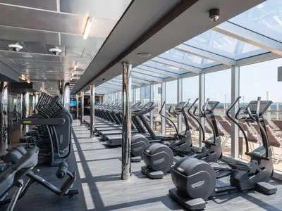 Blick in den großzügigen Fitnessbereich an Bord der MSC Seaview mit Reihen moderner Technogym Laufbänder und Ellipsentrainer. Große Fensterfronten bieten Meerblick, während Tageslicht hereinströmt.