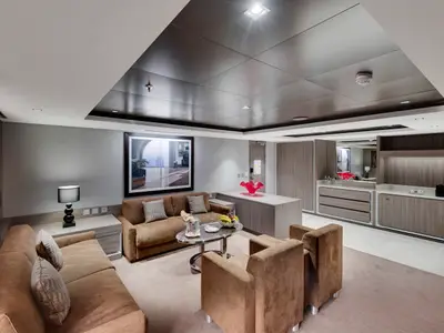 Geräumiger Wohnbereich einer Suite an Bord der MSC Seaview. Braune Sofas und Sessel, ein Tisch mit Sekt und Früchten, Minibar und Wandkunst prägen den eleganten Raum.