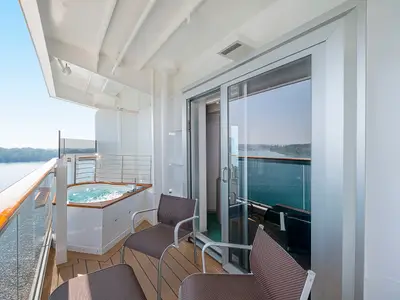 Der private Balkon einer Aurea Premium Suite mit Whirlpool und Lounge-Stühlen an Bord der MSC Seaview. Im Hintergrund weite Sicht auf das Meer und eine grüne Küstenlandschaft.