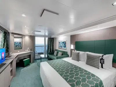Helle Premium Suite Aurea an Bord der MSC Seaview. Doppelbett mit grünem Läufer, grüne Couch, Schreibtisch mit TV. Balkon mit Meerblick. Modernes Interieur in Grün- und Holztönen.