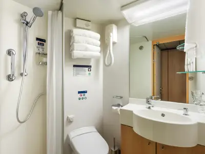 Ein helles und funktionales Badezimmer an Bord der MSC Sinfonia mit einer Duschkabine, einer Toilette und einem Waschbecken mit großem Spiegel. Weiße Handtücher liegen bereit.
