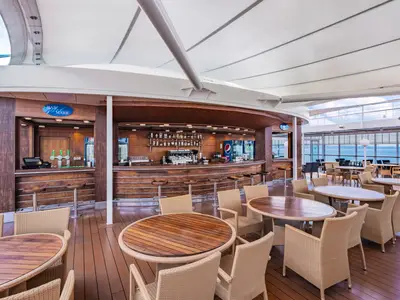 Die Aussenbar Bar Mare auf der MSC Sinfonia mit geschwungener Holztheke, Korbstühlen, Holztischen und Blick auf das weite Meer.
