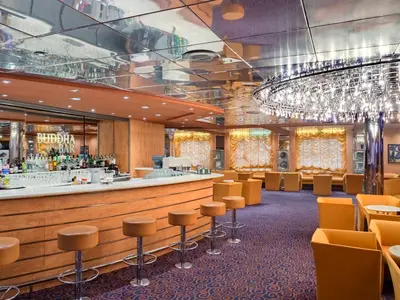 Die Buddha Bar an Bord der MSC Sinfonia. Lange Bar mit Hockern, Spirituosen. Orange Sessel und Sofas in der Lounge. Glänzende Decke mit auffälliger Lichtinstallation.