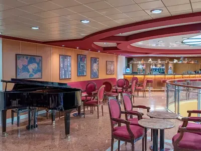 Elegante Bar-Lounge der MSC Sinfonia. Schwarzer Flügel, rote Sessel, Bar mit Hockern, Kunst an Wänden. Rot-weisse Decke. Gläserne Balustrade zum unteren Deck.