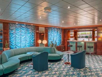 Manhattan Bar an Bord der MSC Sinfonia: Langer Bartresen, blaue Sofas und Sessel. Elegantes Interieur mit Holzpaneelen und blauen gerafften Vorhängen. Ohne Personen.