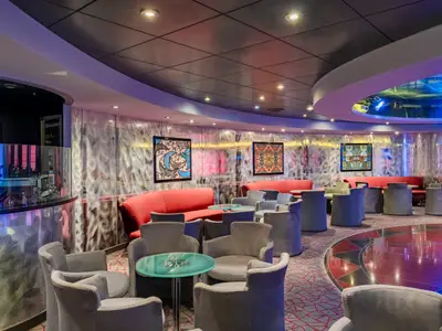 Ein bunter, modern gestalteter Barbereich mit rotem Sofa, grauen Sesseln und einem runden, beleuchteten Tanzbereich an Bord der MSC Sinfonia.