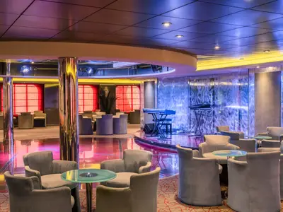 Innenansicht der modernen Sinfonia Lounge an Bord der MSC Sinfonia. Bühne mit Musikinstrumenten, Tanzfläche und zahlreiche Sesselgruppen mit Tischen laden unter farbiger Beleuchtung zum Verweilen ein.