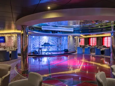 Die Sinfonia Lounge & Library an Bord der MSC Sinfonia bei Nacht. Eine leere Tanzfläche in Pink, eine Bühne mit Keyboard und Sitzbereiche sind sichtbar.