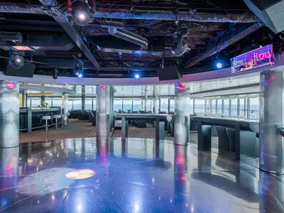 Der Pasha Club Disco an Bord der MSC Sinfonia. Glänzende Tanzfläche mit bunten Lichtern, Bar und moderne Sitzbereiche. Große Fenster mit Meerblick. Eine festliche Atmosphäre.