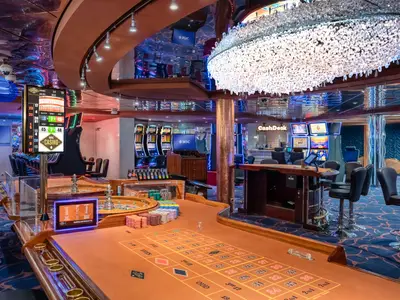 Das glamouröse Sanremo Casino an Bord der MSC Sinfonia, komplett mit glitzerndem Kronleuchter, eleganten Roulette-Tischen, Jetons und leuchtenden Spielautomaten. Ein CashDesk-Schalter ist im Hintergrund zu sehen.