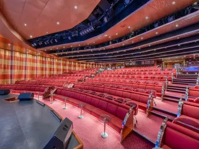 Großer Theatersaal, Teatro San Carlo, an Bord der MSC Sinfonia mit rotem Teppichboden, roten gepolsterten Sitzreihen und einer dunklen Bühne. Die Decke ist teilweise rot mit Sternenlicht, teilweise schwarz mit Bühnenbeleuchtung.