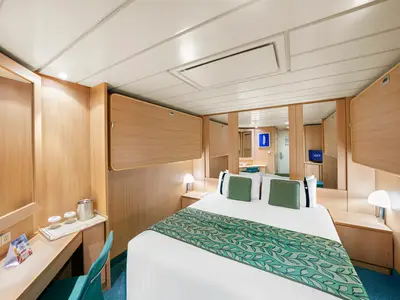 Geräumige Innenkabine an Bord der MSC Sinfonia mit Doppelbett, grünen Kissen, hellem Holzinterieur und einem kleinen Schreibtisch.