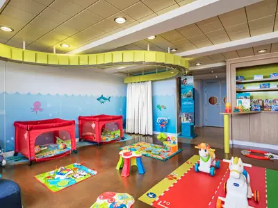 Heller Baby Club der MSC Sinfonia mit roten Reisebetten, bunten Spielmatten und vielen Spielsachen. Die Wände sind kinderfreundlich mit Meeresmotiven gestaltet.