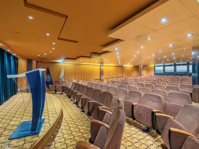 Blick in den Konferenzraum an Bord der MSC Sinfonia. Der Raum ist mit braunen Sitzen in Reihen und einer Buehne mit Pult ausgestattet. Grosse Fenster geben den Blick auf das weite Meer frei.