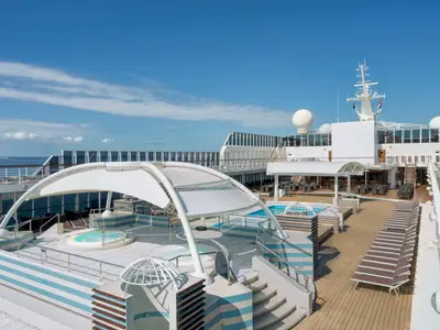 Blick auf den weitläufigen Poolbereich "Le Piscine" an Bord der MSC Sinfonia. Zu sehen sind mehrere Whirlpools unter einem Sonnendach, Liegestühle, eine Bar und das offene Meer.