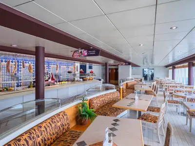 Blick in den hellen Buffetbereich "La Terrazza" an Bord der MSC Sinfonia. Der Raum ist mit Tischen, Stühlen und gemütlichen Sitzbänken ausgestattet und bietet durch große Fenster einen weiten Meerblick. Essensstationen für Wurst- und Käseplatten sowie Backwaren sind zu sehen.
