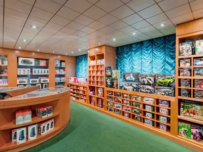 Der Duty-Free-Shop The Mini Mall an Bord der MSC Sinfonia, gefüllt mit Elektronikartikeln und LEGO-Sets. Holzeinrichtung, blaue Vorhänge und grüner Teppichboden schaffen ein helles Einkaufserlebnis.