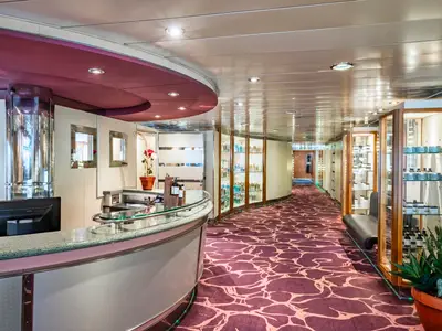 Die moderne Rezeption des MSC Aurea Spa an Bord der MSC Sinfonia. Ein geschwungener Tresen, Glasvitrinen mit Pflegeprodukten und ein purpurroter Teppich prägen den hellen Flur.