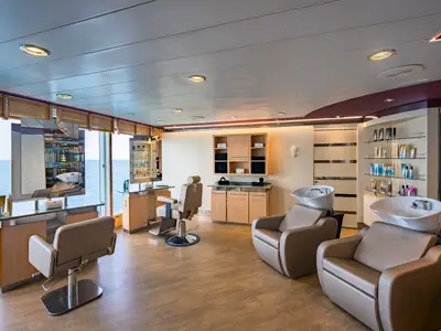 Moderner Haarsalon an Bord der MSC Sinfonia. Frisierplätze mit Spiegeln, Produktregale und Haarwaschbecken sind zu sehen. Große Fenster zeigen das offene Meer.