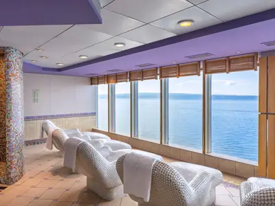 Heller Spa-Entspannungsbereich der MSC Sinfonia mit modernen Liegestühlen und Handtüchern. Große Fenster bieten weiten Meerblick auf den Horizont. Eine Mosaikdusche steht links.