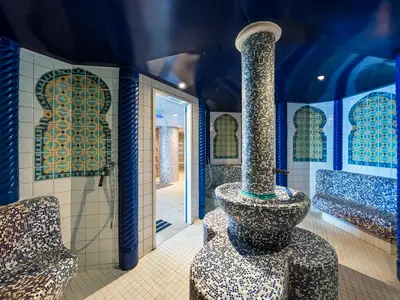 Thermalbereich an Bord der MSC Sinfonia. Blaue und weiße Mosaike auf Wänden, Säulen und Sitzbänken. Zentrale Säule mit Wasserbecken. Gewölbte Decke.