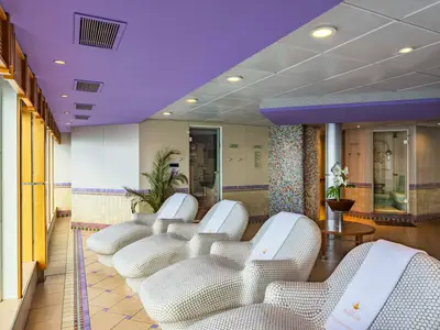 Eine Reihe von Liegestühlen im Entspannungsbereich des MSC Aurea Spa an Bord der MSC Sinfonia. Im Hintergrund sind Eingänge zu Thermalbereichen mit Mosaikfliesen und Pflanzen zu sehen.