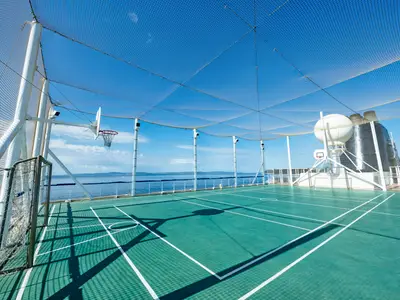 Multifunktions-Sportplatz auf der MSC Sinfonia. Grünes Feld mit Basketballkorb, Fußballtor und Schutznetzen. Blauer Himmel über dem Meer im Hintergrund.