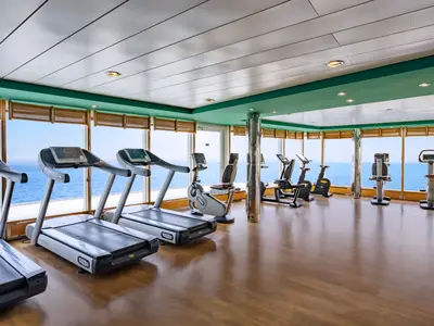 Ein geräumiges Fitnessstudio an Bord der MSC Sinfonia mit zahlreichen Laufbändern und Fahrrädern mit Blick auf das offene Meer.