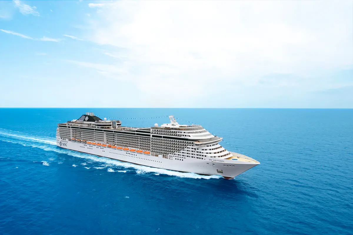 Die MSC Splendida gleitet majestätisch über tiefblaues Meer unter klarem Himmel. Das Kreuzfahrtschiff ist von oben und leicht schräg von vorne sichtbar und zieht eine weiße Bugwelle.