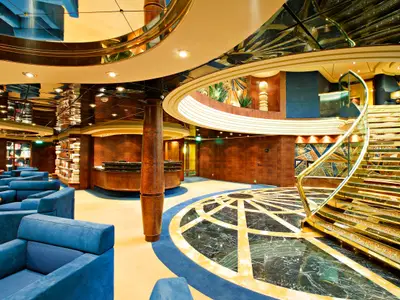 Blick in das luxuriöse Atrium der MSC Splendida. Eine Rezeption, blaue Sessel und eine goldene Wendeltreppe dominieren den eleganten Innenraum mit dunklem Holz und glänzenden Oberflächen.