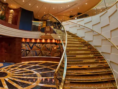 Die prunkvolle goldene Swarovski-Treppe an Bord der MSC Splendida führt elegant nach oben, umgeben von edlen Materialien und kunstvoller Beleuchtung. Unten ein kunstvoller Marmorboden.