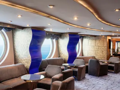 Die elegante L'Aperitivo Bar-Lounge an Bord der MSC Splendida. Helle Sitzecken mit Sofas und Sesseln, moderne Wandgestaltung und große Bullaugen mit weitem Meerblick.