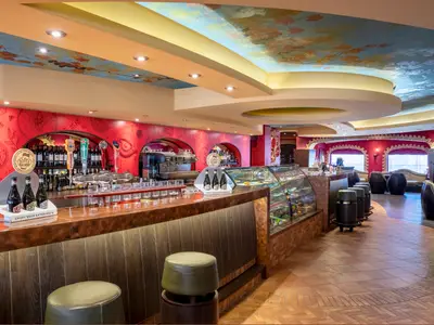 Der L'Enoteca Bar auf der MSC Splendida zeigt eine lange Theke mit Zapfhähnen, Flaschen und Gläsern. Im Hintergrund rote Wände mit asiatischen Mustern und eine gemalte Decke. Sitzbereiche laden zum Verweilen ein.