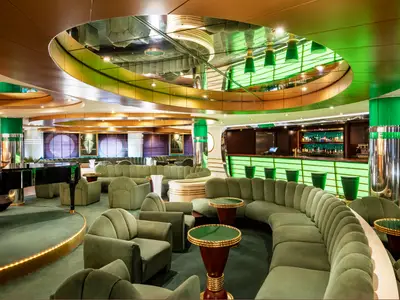 Blick in die La Prua Piano Bar an Bord der MSC Splendida mit vielen grünen Samtsesseln und Sofas sowie einem schwarzen Flügel im Vordergrund und einer leuchtend grünen Bar im Hintergrund. Der Raum hat eine elegante Atmosphäre mit glänzenden Oberflächen und indirekter Beleuchtung.
