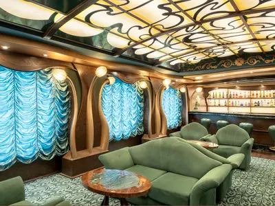 Eine luxuriöse Bar-Lounge an Bord der MSC Splendida. Grüne Sessel und Sofa, eine Bar mit vielen Flaschen und eine kunstvolle, beleuchtete Decke im Art Nouveau-Stil sind zu sehen.