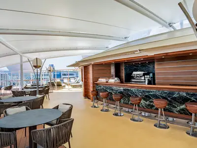 Elegante Outdoor-Bar, The One Bar, an Bord der MSC Splendida. Überdachte Marmortheke, Holzverkleidung, bequeme Barhocker und Lounge-Sitzbereiche auf dem Deck.