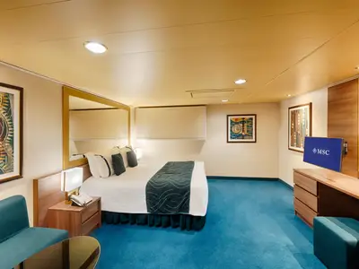 Eine geräumige, barrierefreie Deluxe-Innenkabine an Bord der MSC Splendida mit Doppelbett, blauer Teppichboden, einem Schreibtisch mit Spiegel und Fernseher sowie einem Sofa in Türkis.