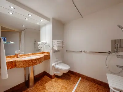 Ein barrierefreies Badezimmer an Bord der MSC Splendida mit einem Waschtisch, WC und einer Dusche mit Klappsitz und Haltegriffen. Der Boden ist marmoriert.